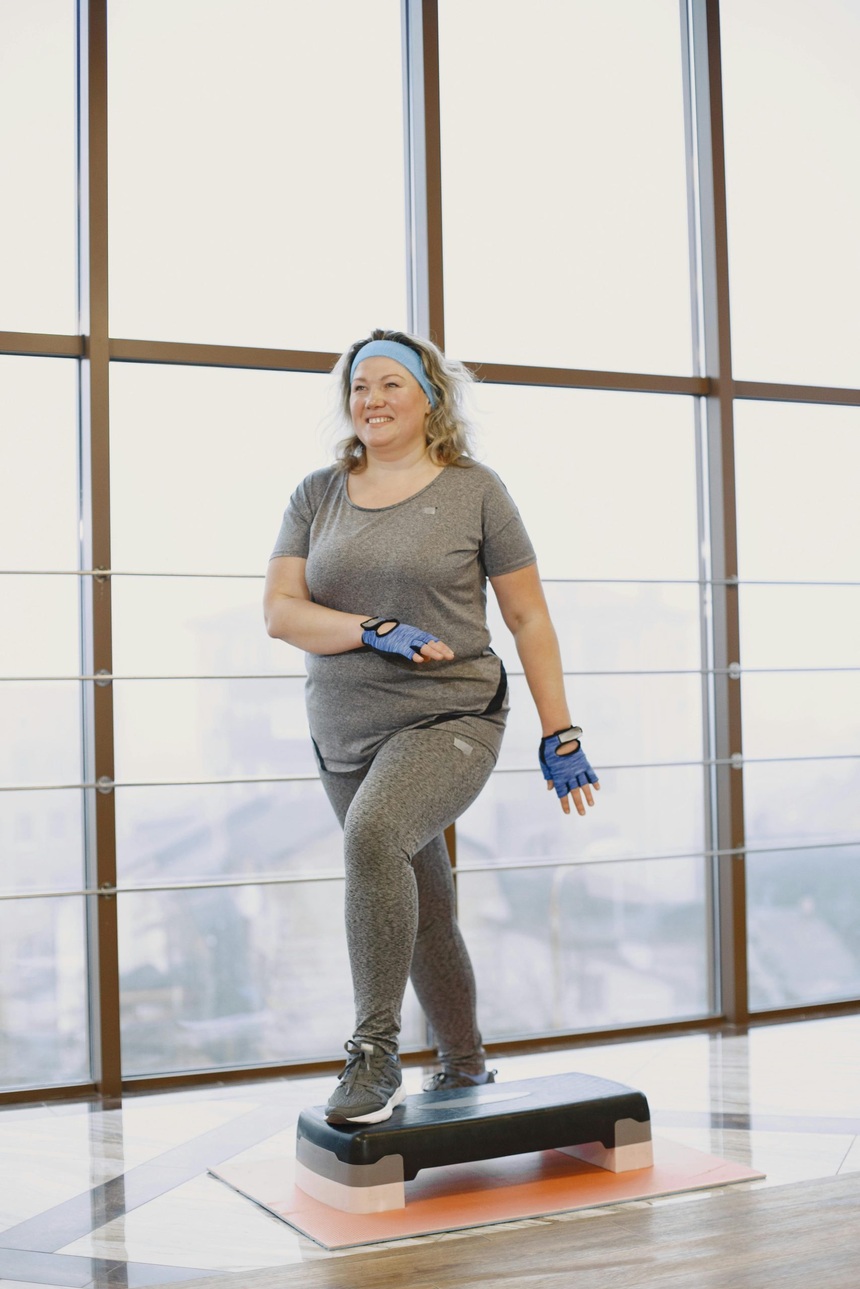 Active middle-aged woman in gym performing step exercise, promoting a healthy lifestyle indoors.