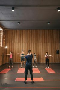 A diverse group of adults stretching together in an indoor fitness class, led by an instructor.