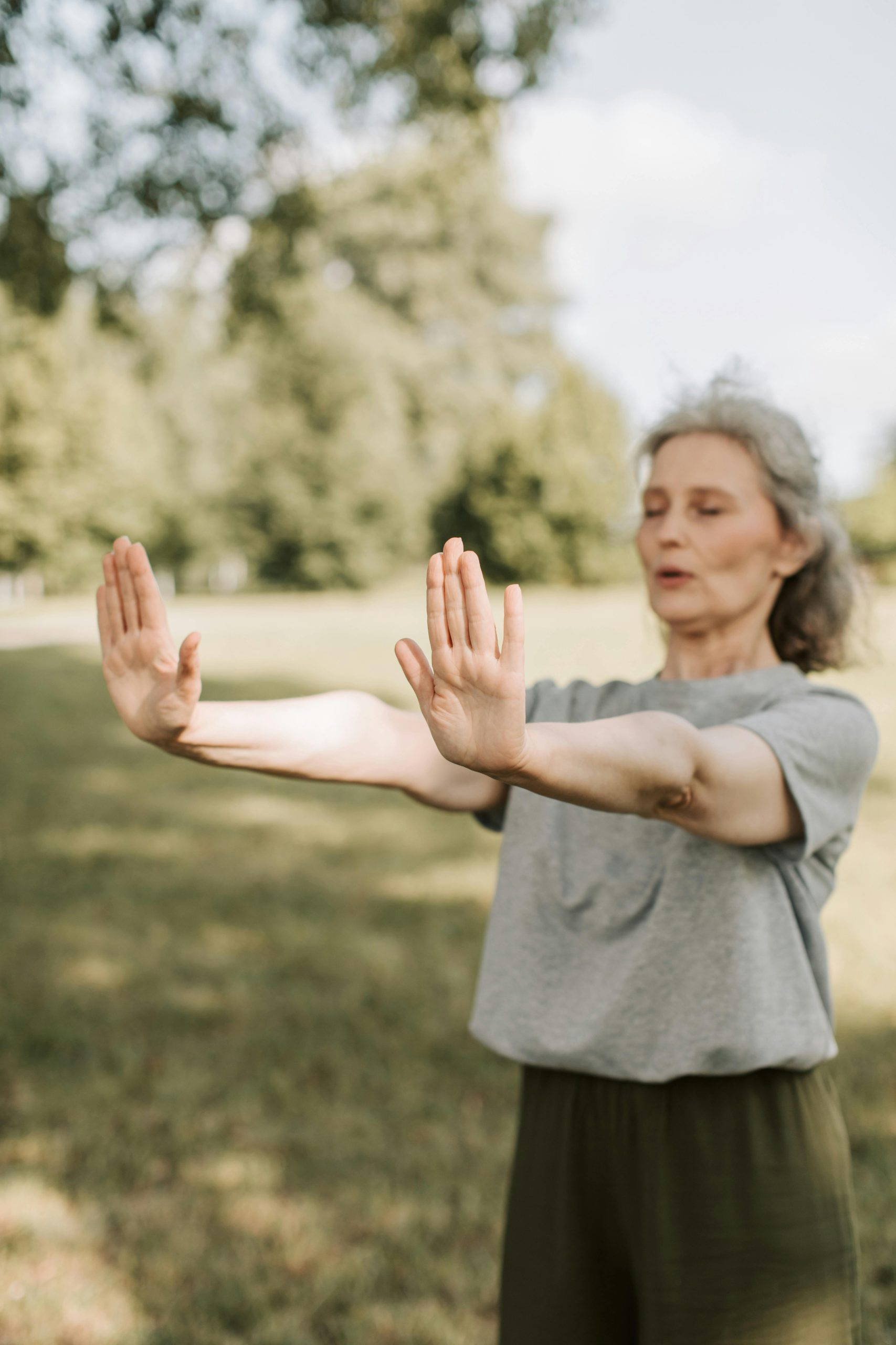Nicole Senior woman practicing Tai Chi in a sunny park, focusing on mindfulness and healthy lifestyle.
